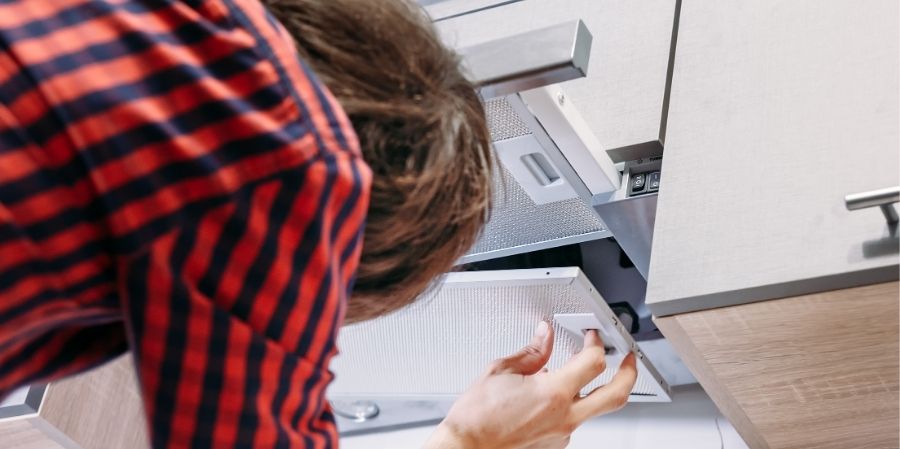 Uomo che controlla l'interno di una cappa aspirante in cucina